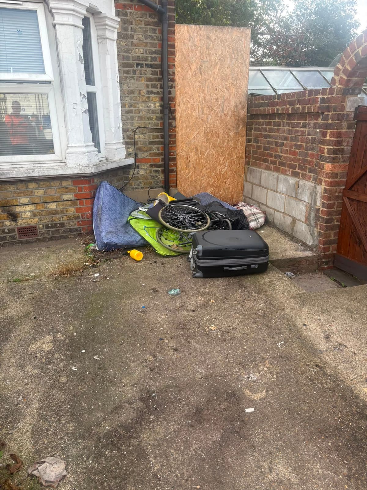 Mattress, wheelchair, suitcase and household rubbish piled in a front drive before rubbish removal