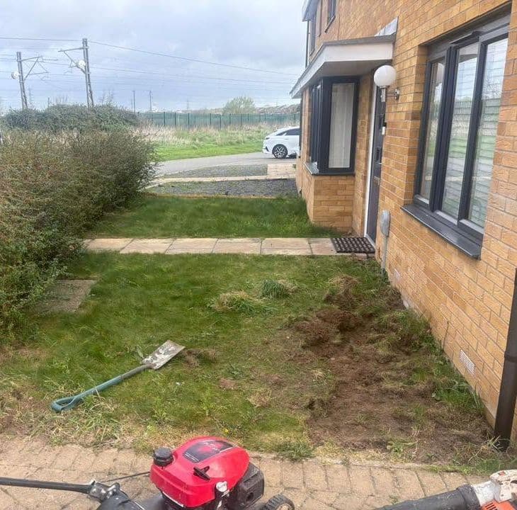 Overgrown front garden with patchy grass and dug-up soil beside a brick house before work began
