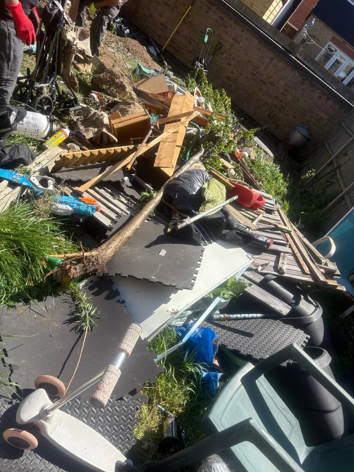 Back garden covered in broken fence panels, timber, toys, rubber matting and garden waste during a clearance