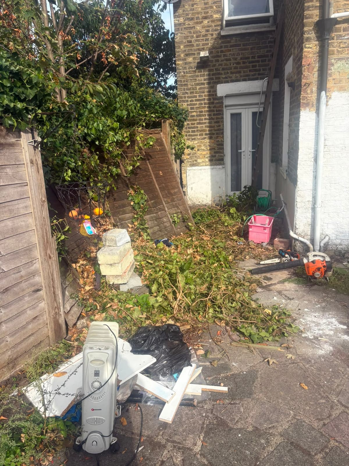 Side garden with hedge trimmings, broken timber, an oil heater and rubbish before garden clearance