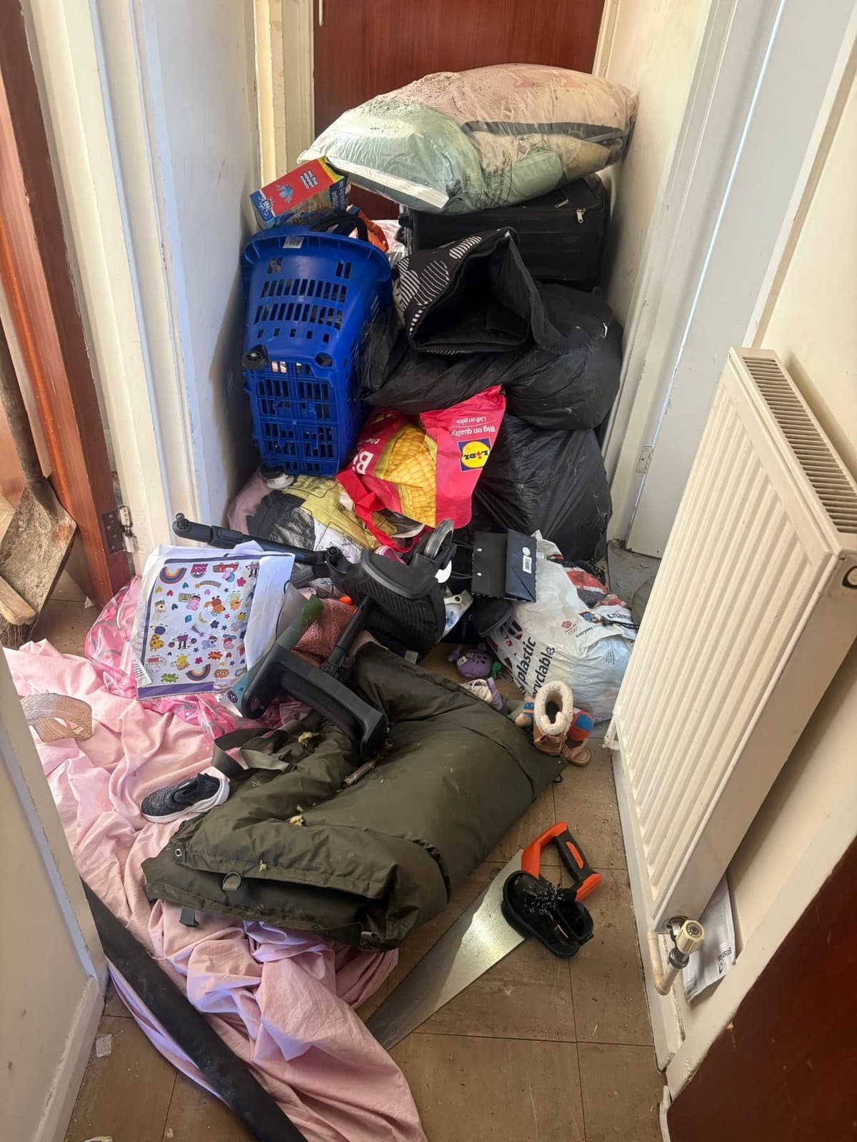 Hallway piled with bin bags, bedding, a laundry basket, shoes and household items before a house clearance
