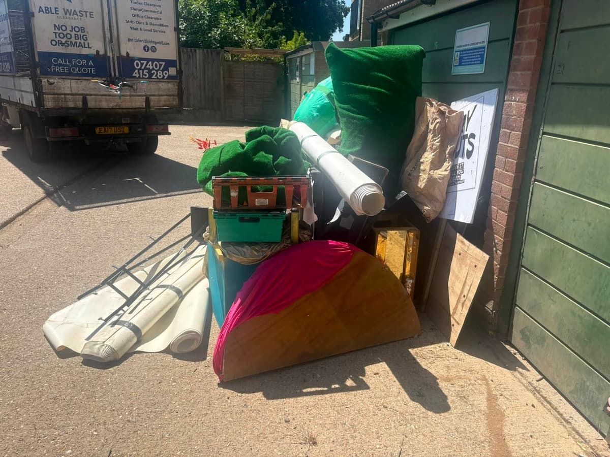 Pile of old furniture, rolled flooring and artificial grass beside a garage block, with the clearance van parked behind